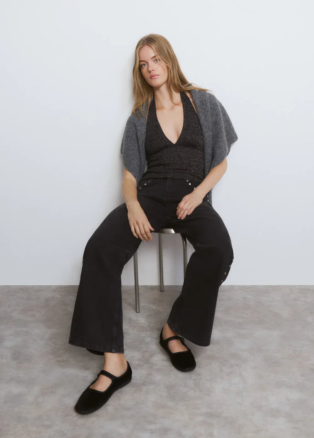 דוגמנית יושבת עם סריג אפור, גופיה שחורה ומכנסיים רחבים, צילומי אופנה CHOZEN