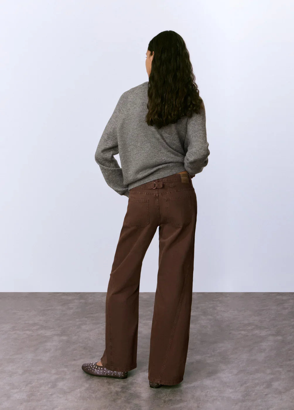 דוגמנית עם סוודר אפור ומכנסיים חומים רחבים מבית CHOZEN, צילום אופנה על רקע נייטרלי