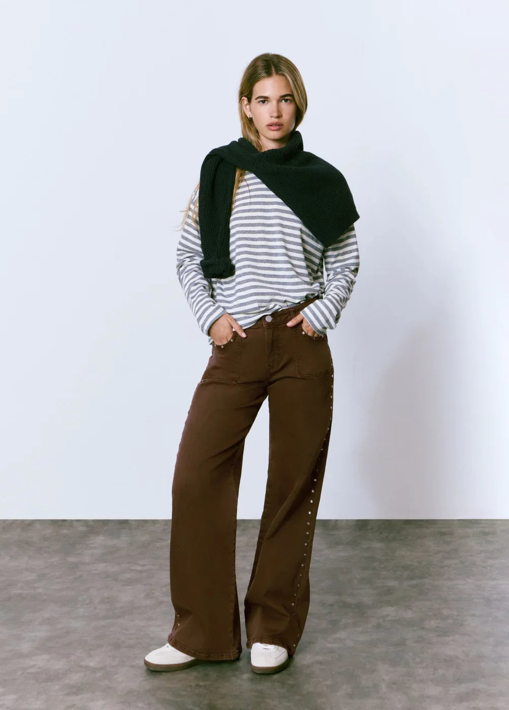 דוגמנית עם חולצת פסים אפורה, מכנסי קז'ואל חומים ונעליים לבנות בית CHOZEN