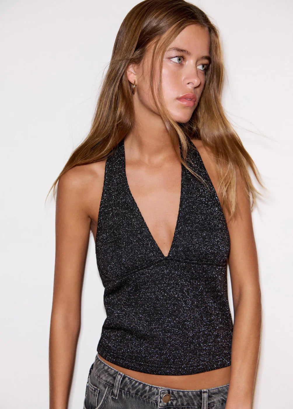 אישה לובשת טופ שחור מנצנץ עם מפתח עמוק מבית CHOZEN, צילום אופנה על רקע לבן