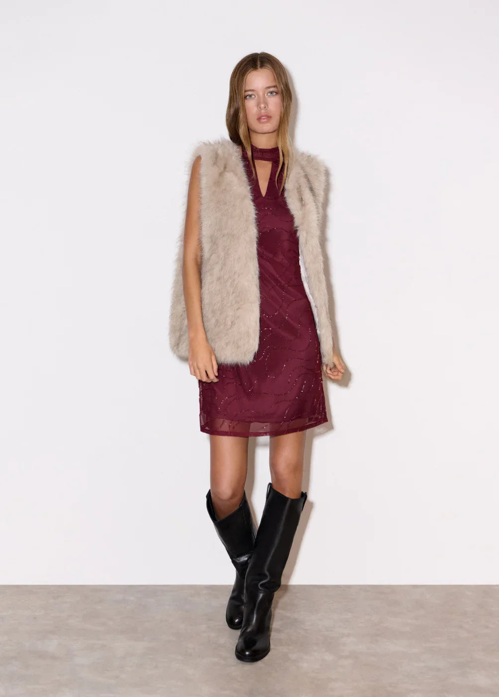 דוגמנית לובשת שמלה סגולה ללא שרוולים, וסט פרווה בהיר ומגפיים שחורים, אופנה טרנדית CHOZEN