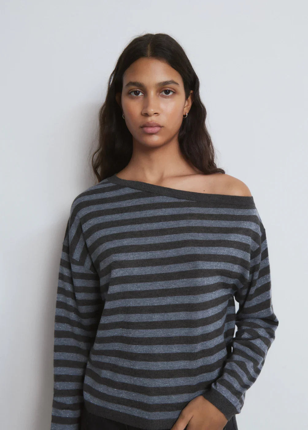 אישה לובשת סוודר פסים אפור ושחור, אופנה CHOZEN, צילום פנים מול קיר לבן