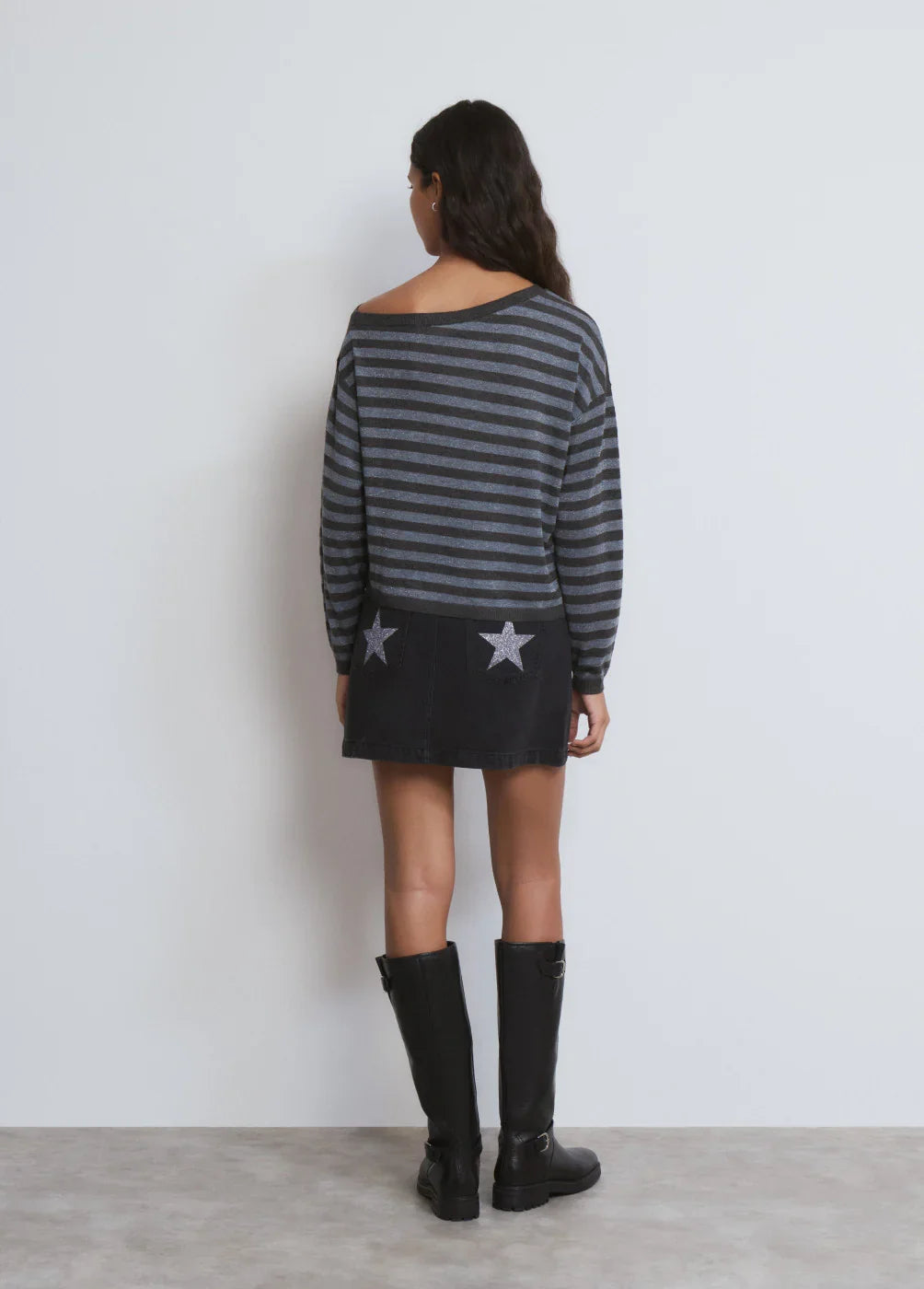 אישה לובשת סוודר פסים אפור-שחור וחצאית שחורה עם כוכבים, מגפיים שחורים, אופנה CHOZEN