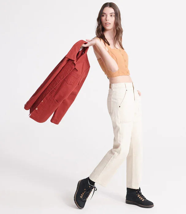 דוגמנית באופנת CHOZEN, טופ כתום, מכנסיים לבנים, נעליים שחורות ומעיל אדום ביד