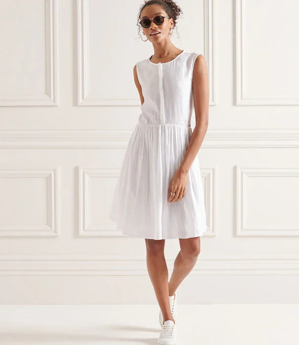 אישה עומדת לובשת שמלה לבנה ללא שרוולים, משקפי שמש ונעלי סניקרס, צולם באווירה אלגנטית בחנות CHOZEN