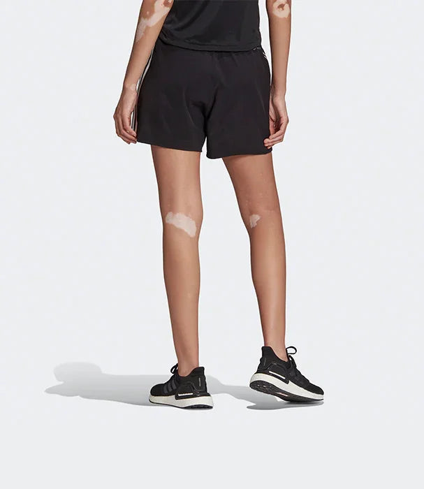 דגם לובשת מכנסיים קצרים שחורים ונעלי ספורט שחורות על רקע לבן, אופנת ספורט CHOZEN