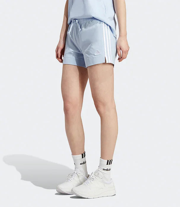 דגם לובשת מכנסי ספורט קצרים של אדידס בגוון תכלת עם פסים לבנים, נעלי אדידס, ב-CHOZEN