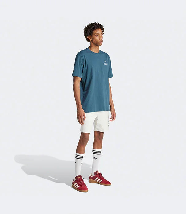 גבר לובש טישרט כחולה, מכנסיים קצרים לבנים, גרביים גבוהות ונעלי ספורט אדומות, רקע חלק, אופנת גברים CHOZEN