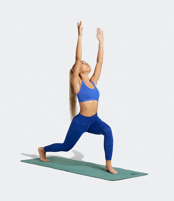 אשה עושה יוגה בבגדי ספורט כחולים על מזרן, צילום לאתר CHOZEN, אופנת כושר