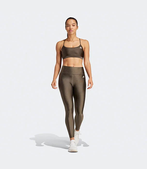 אישה בדגם הלבשה ספורטיבית של אדידס בצבע אפור, לבושה בטייץ וחזיית ספורט, על רקע לבן