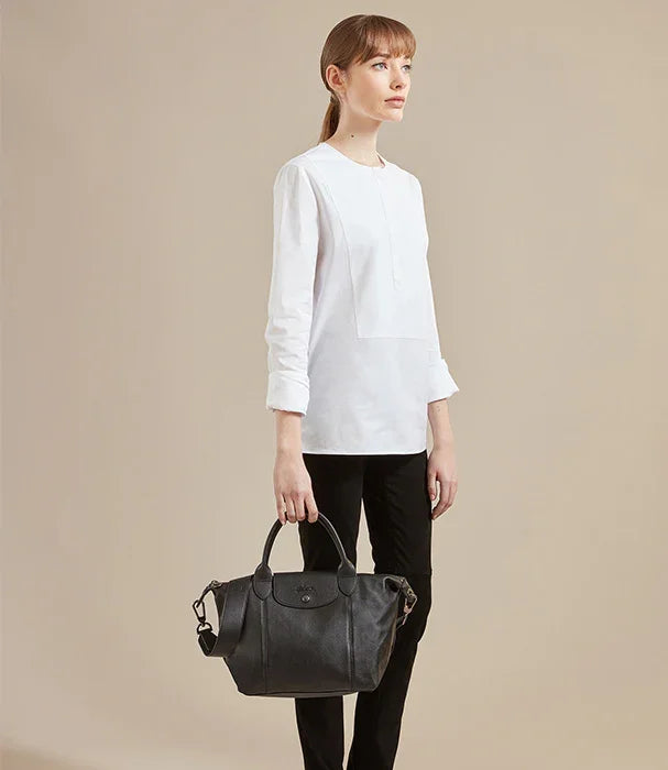 אישה עם חולצה לבנה ומכנסיים שחורים מחזיקה תיק יד שחור, צילום סטודיו לקבוצת אלפא CHOZEN