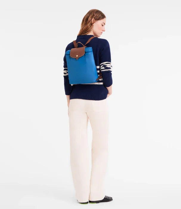 אישה עם תיק גב כחול אופנתי, לבושה בסוודר כהה ומכנסיים בהירים, מותגי CHOZEN