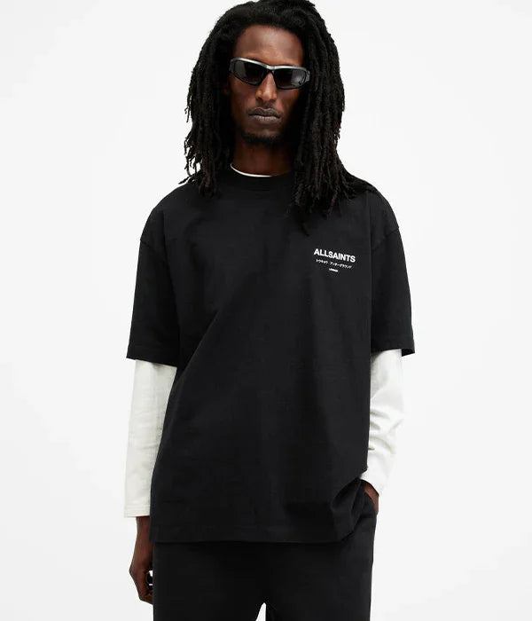 גבר עם משקפי שמש לובש חולצת טי שחורה עם הדפס ALLSAINTS על רקע לבן
