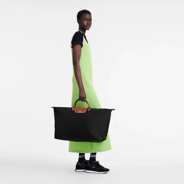 אישה בשמלה ירוקה מחזיקה תיק גדול שחור עם ידיות חומות, רקע לבן נקי, CHOZEN מותגים מובילים