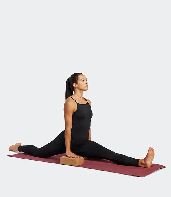 אישה בבגד ספורט שחור עושה שפגת על מזרן יוגה עם קוביית תרגול, אופנת כושר CHOZEN