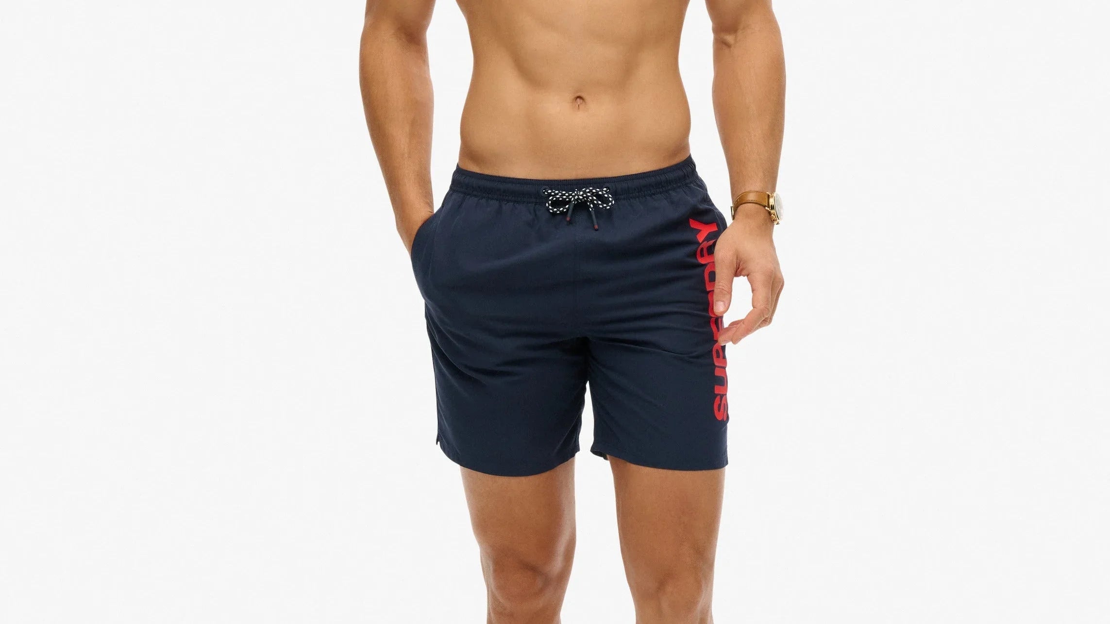 דגם גבר לובש מכנסי בגד ים קצרים בצבע כחול עם לוגו SUPERDRY, אופנת גברים CHOZEN