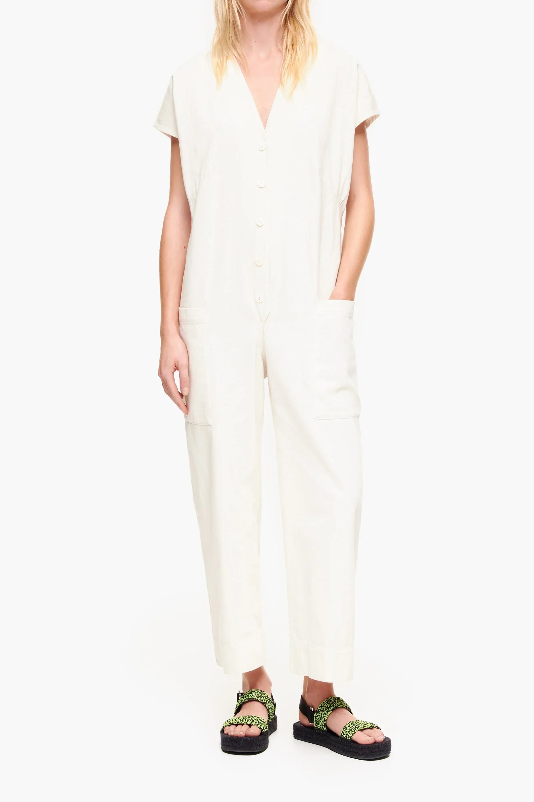אישה לובשת אוברול אוף-ווייט עם שרוולים קצרים וכפתורים, וסנדלים שחורים עם רצועות ירוקות, צילום לקטגוריית בגדי נשים ב-CHOZEN