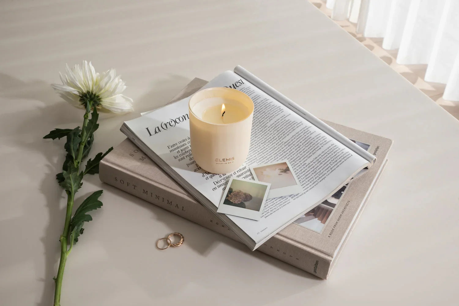 נר ELEMIS דולק על מגזין וספר, צמח, שתי טבעות ותמונות פולארויד בעיצוב מינימליסטי, CHOZEN