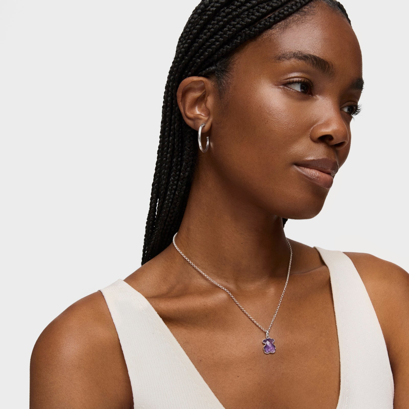 אישה עונדת שרשרת עם תליון סגול ועגיל חישוק כסף, חולצה לבנה, רקע ניטרלי