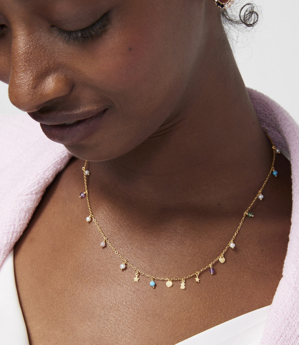 אישה עונדת שרשרת זהב עם תליוני פנינים ואבני חן צבעוניות על רקע לבן