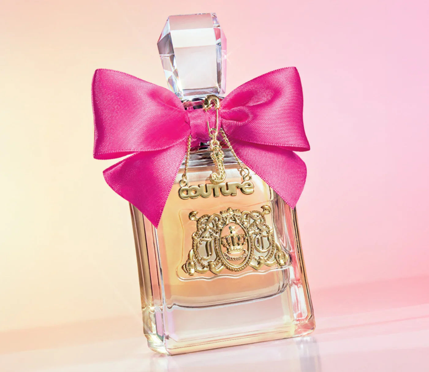 בקבוק בושם יוקרתי עם פקק קריסטל סרט ורוד וקישוטי זהב רקע בגווני ורוד וכתום
