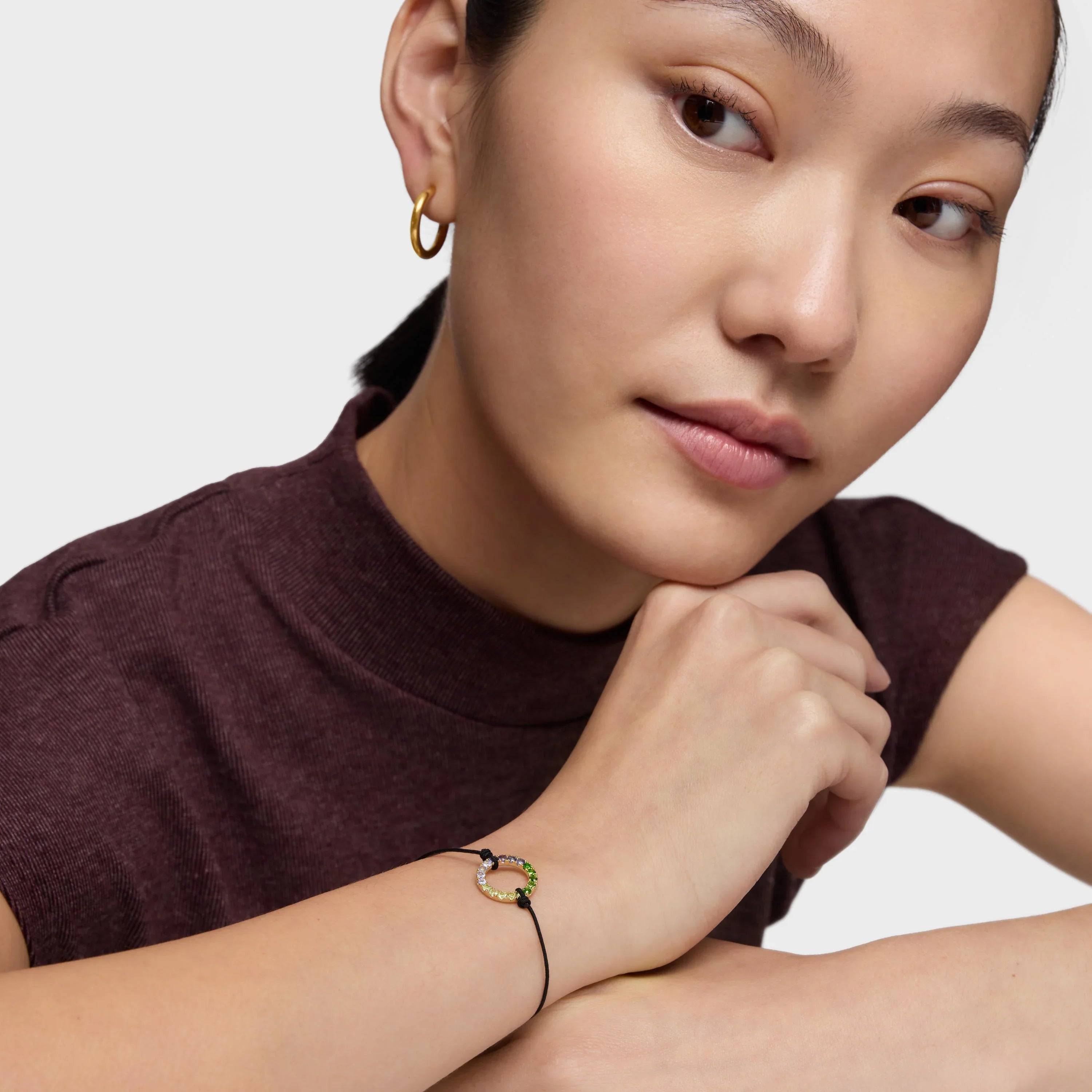 אישה עונדת צמיד חוט שחור עם תליון עגול משובץ אבני חן, עגיל חישוק זהב