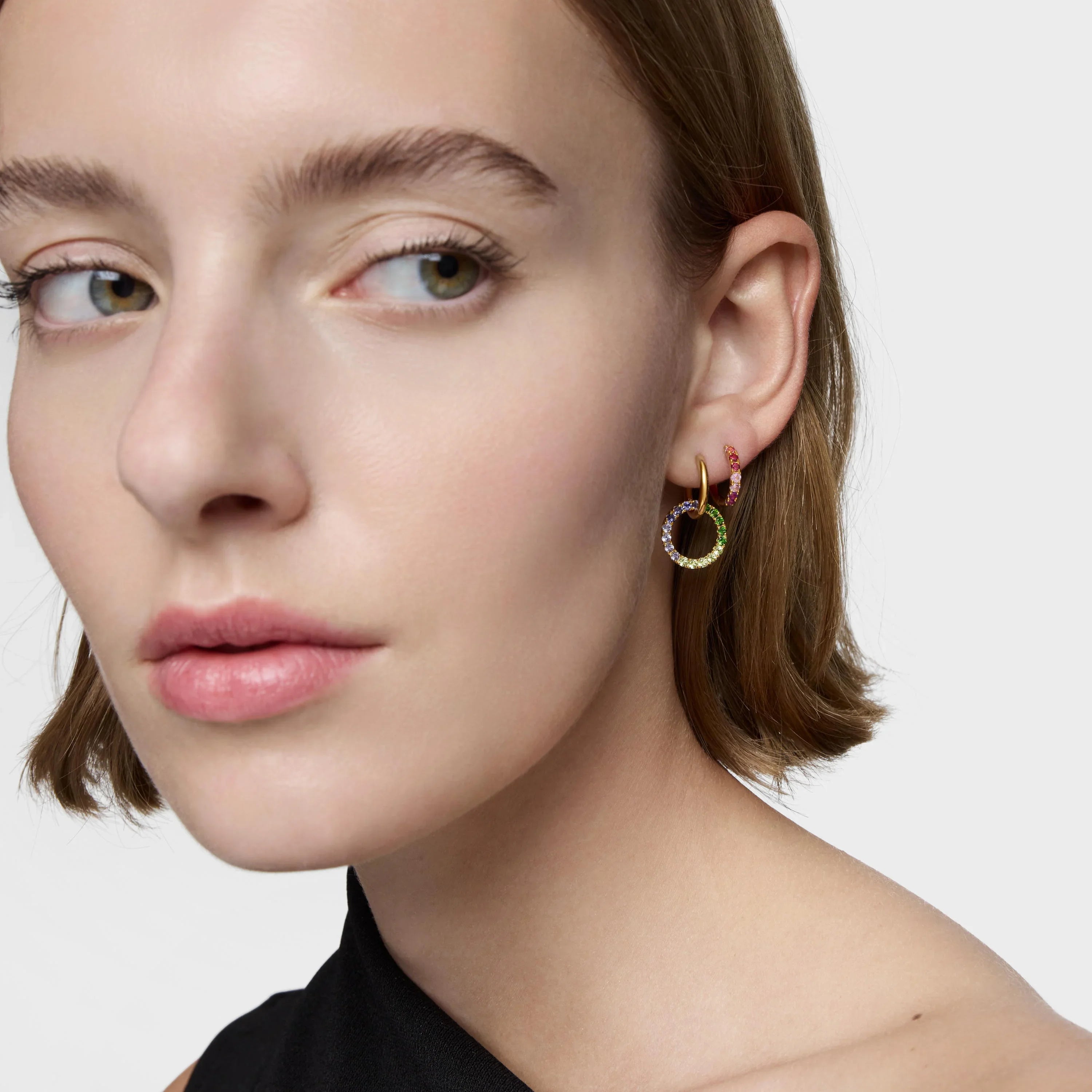 דוגמנית עונדת עגילי חישוק עם אבני חן צבעוניות, תקריב על הפנים