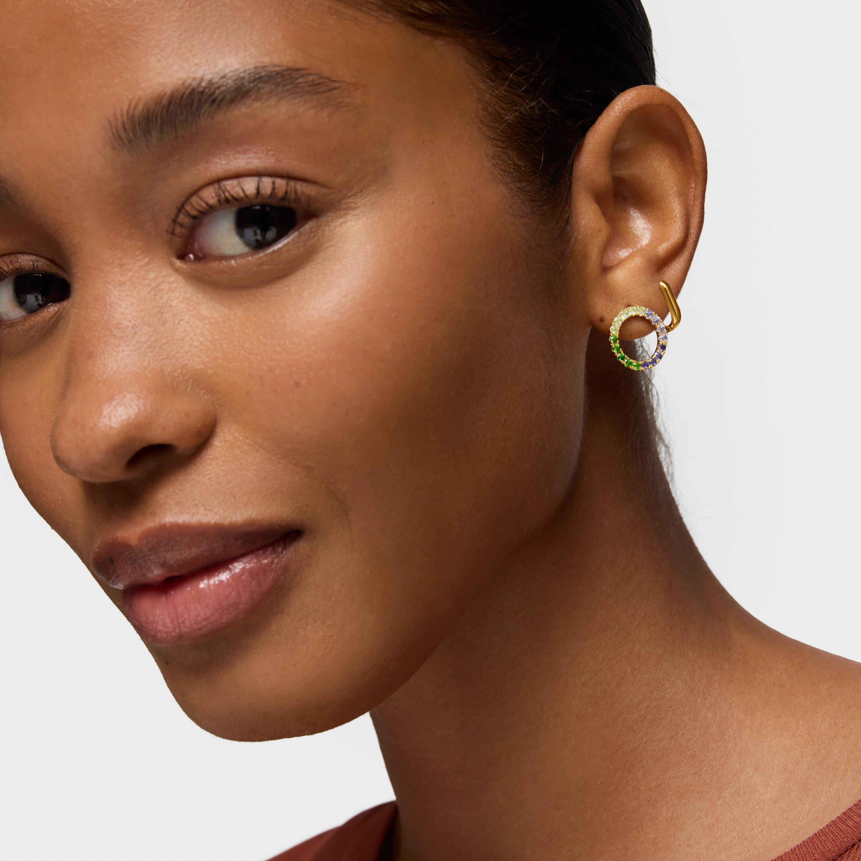 אישה עונדת עגיל זהב עגול עם אבני חן צבעוניות על רקע לבן