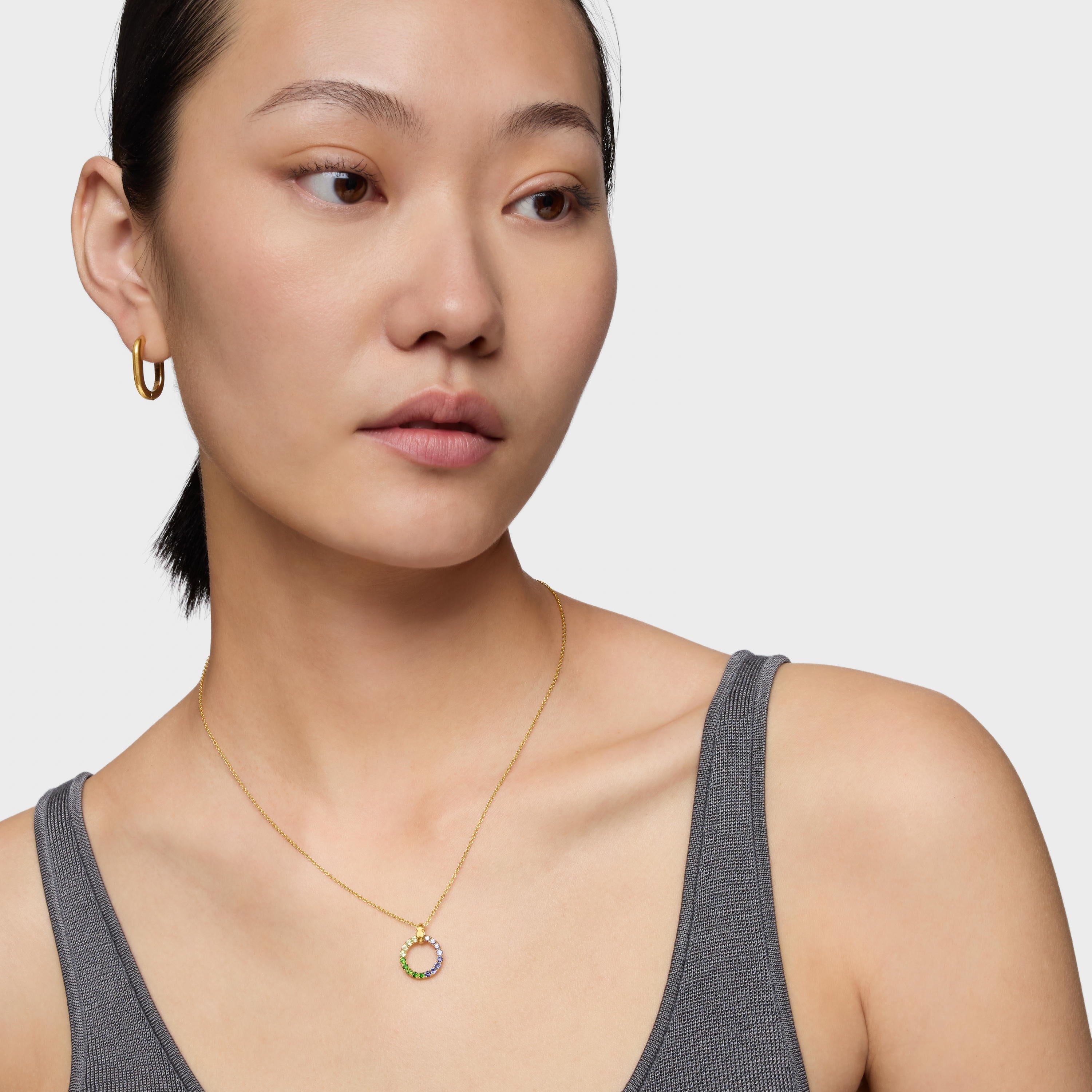 אישה עונדת שרשרת זהב עם תליון עגול משובץ אבנים צבעוניות ועגיל חישוק זהב