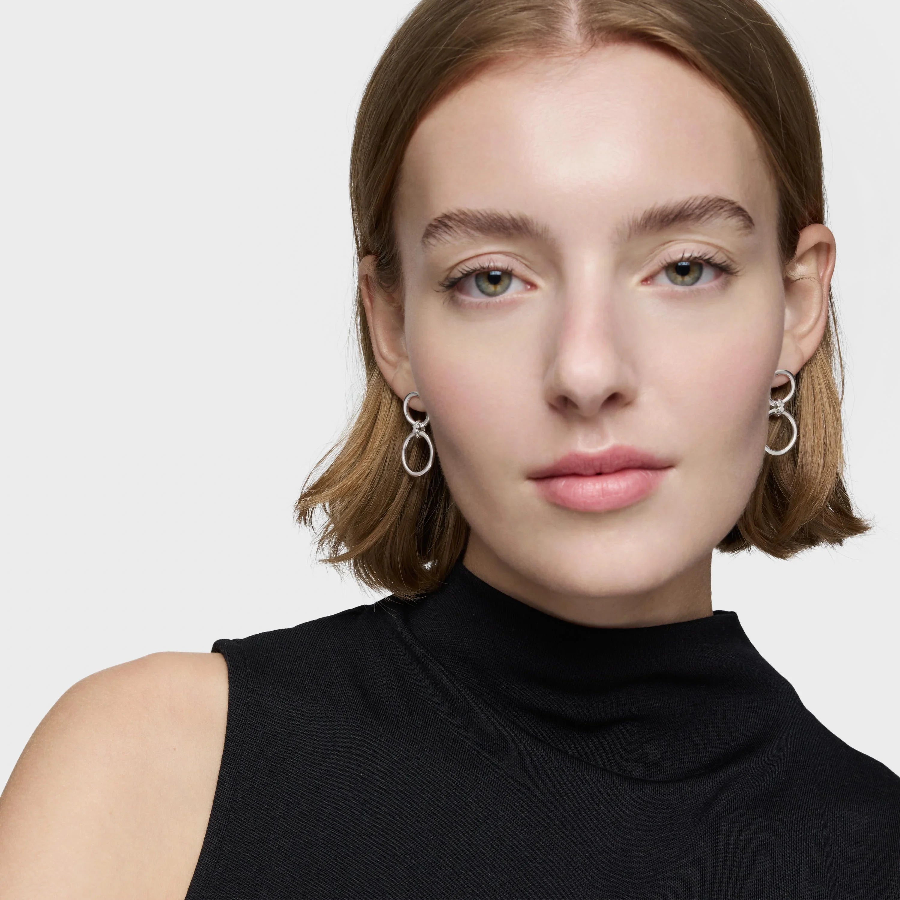 אישה עם שיער בלונדיני קצר עונדת עגילי כסף מעוצבים בלבוש אלגנטי שחור