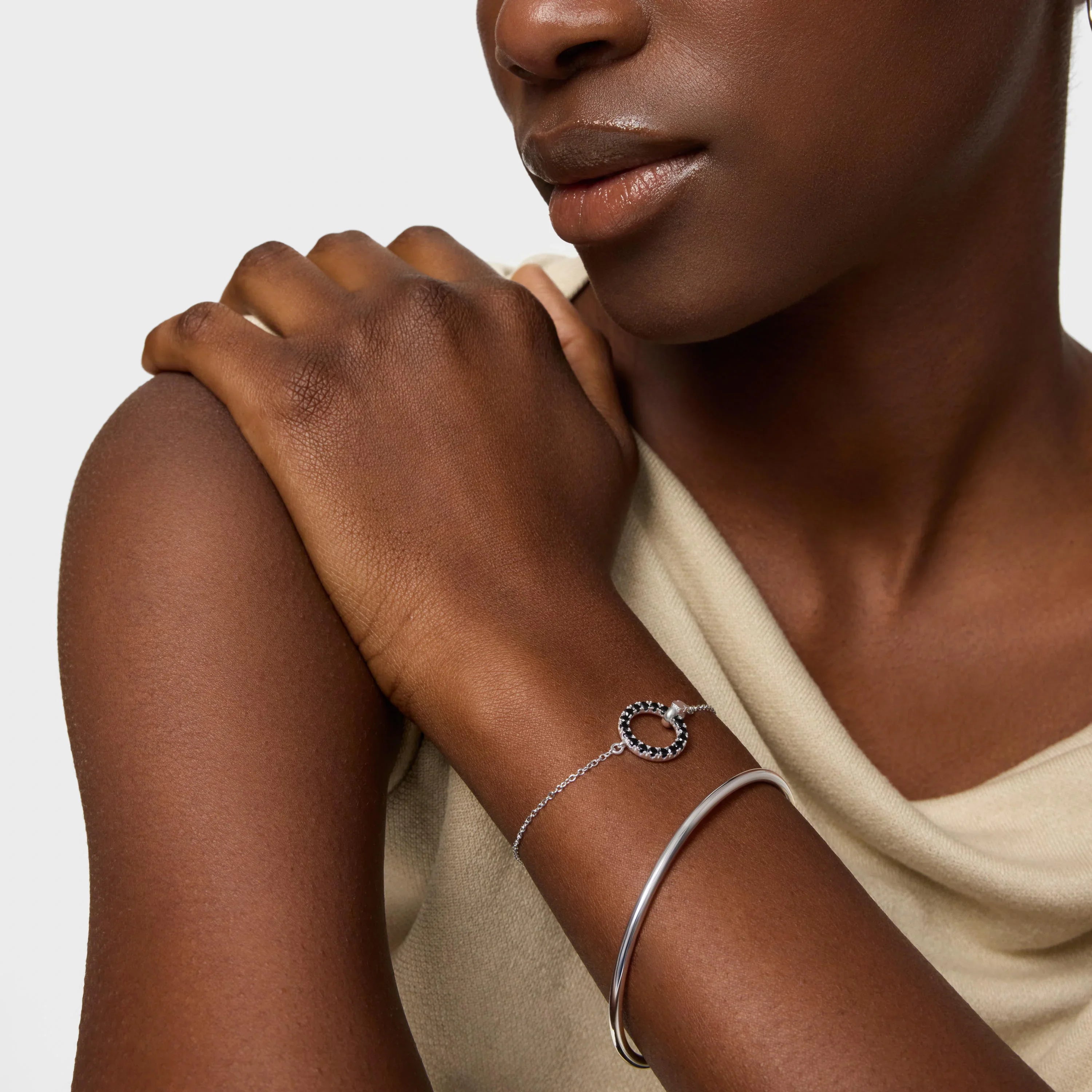 אישה עונדת צמיד כסף עדין עם תליון עיגול משובץ לצד צמיד כסף קשיח, תכשיטים אופנתיים