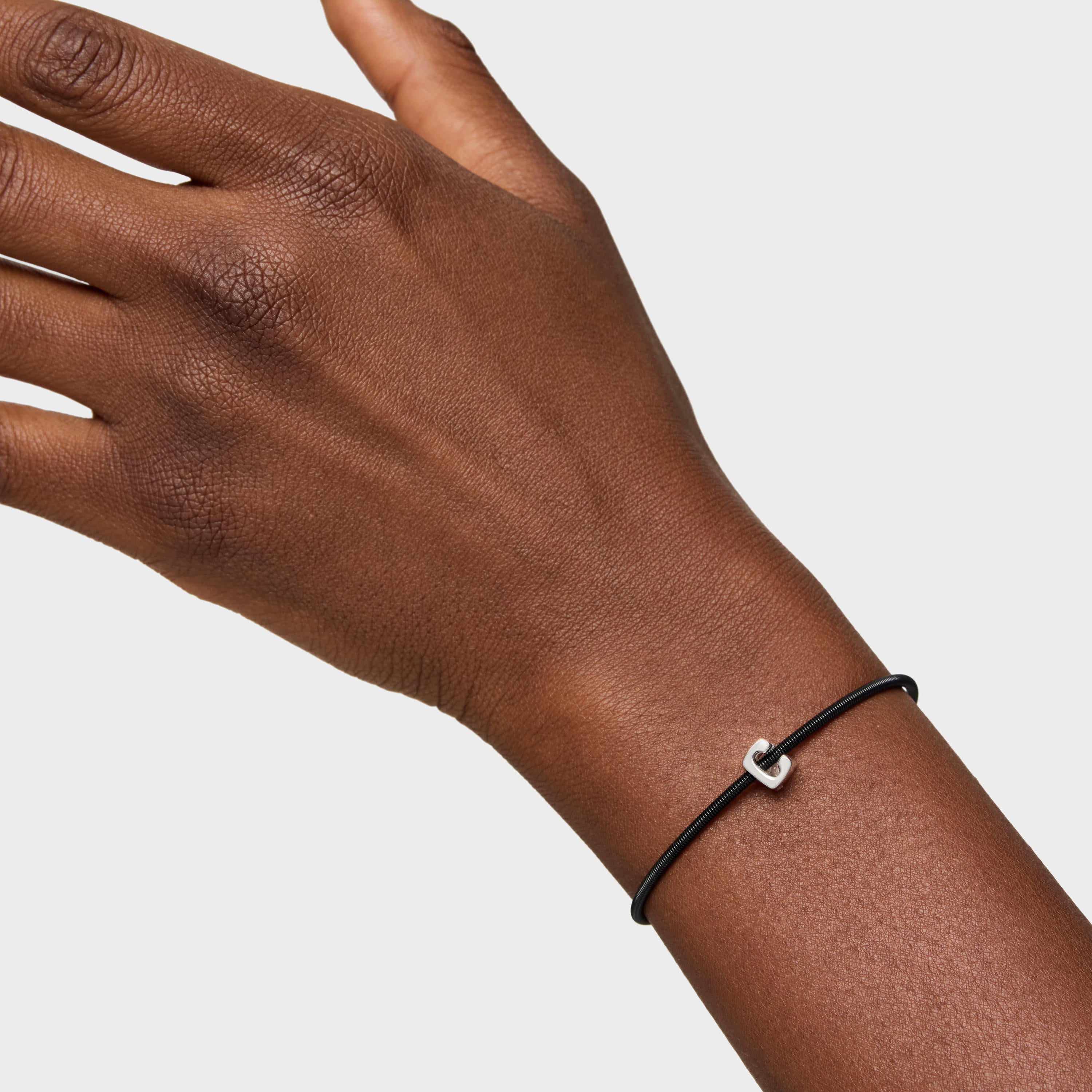 יד עם צמיד שחור עדין ותליון מתכת קטן, רקע לבן, תכשיטי אופנה