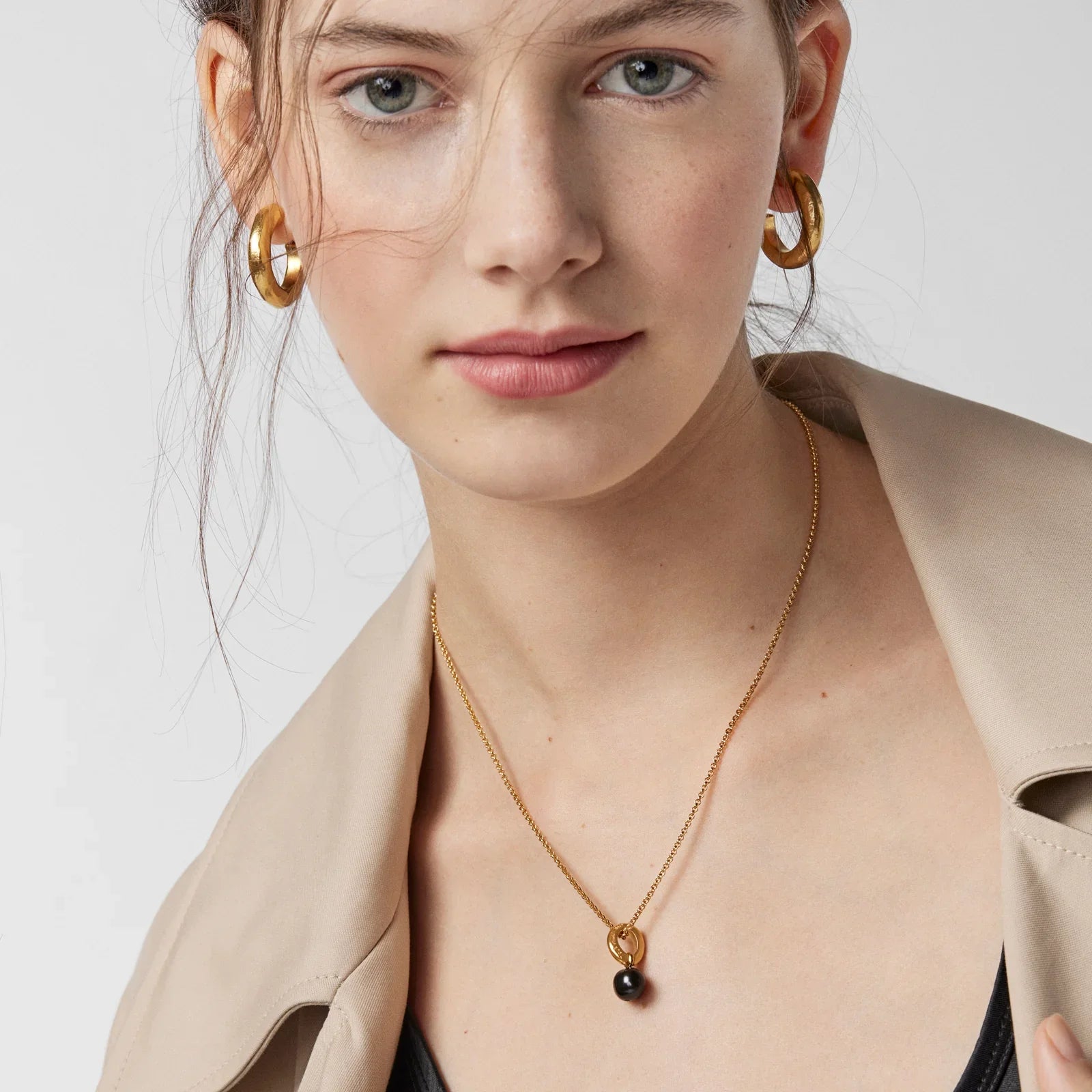 אישה עונדת עגילי חישוק זהב ושרשרת זהב עם תליון שחור, צילום תקריב, CHOZEN תכשיטים יוקרתיים