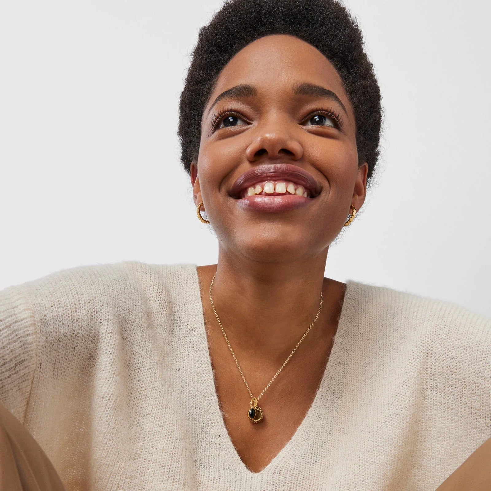 אישה מחייכת עם שרשרת זהב, עגילים וסוודר קרמי, מותגי אופנה CHOZEN