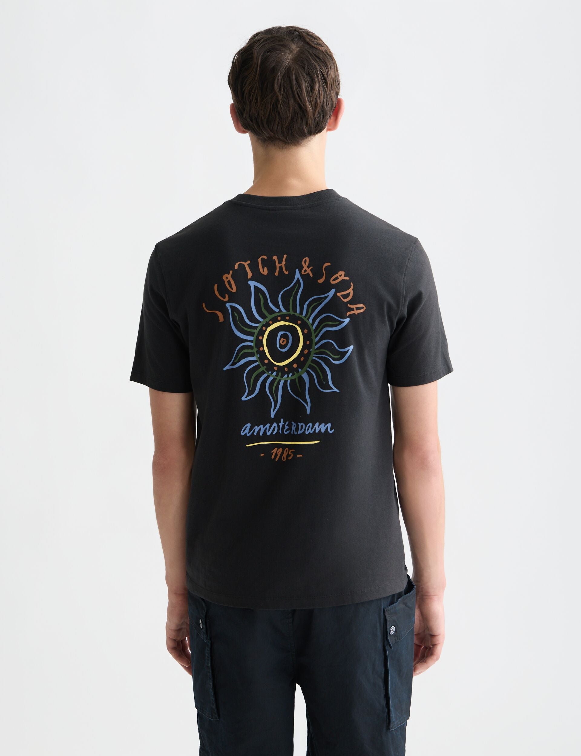 גבר לובש חולצת טי שחורה עם הדפס צבעוני של Scotch & Soda אמסטרדם, מבית CHOZEN