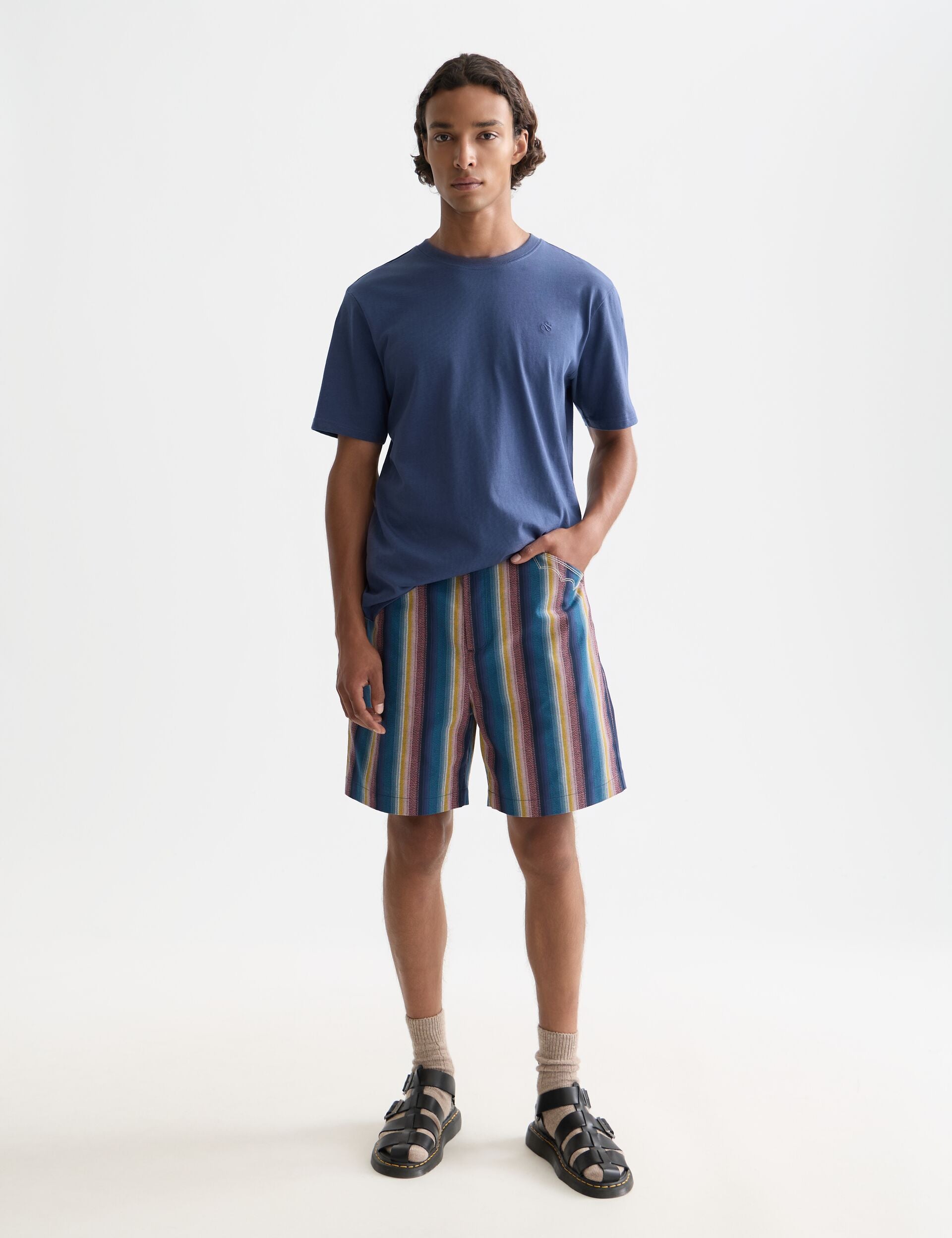 דגם גבר לובש חולצת טי כחולה ומכנסיים קצרים מפוספסים, אופנה עדכנית באתר CHOZEN