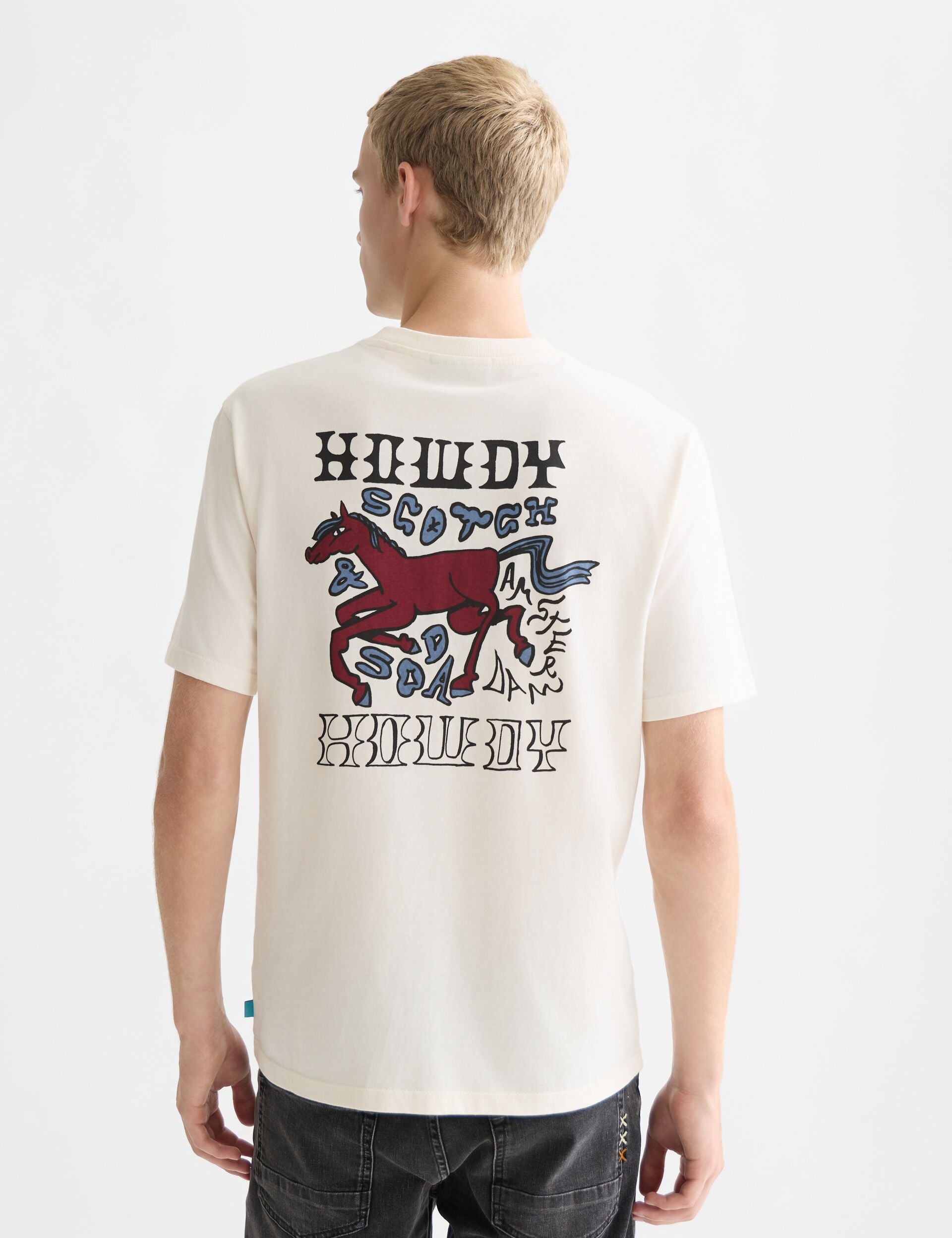 גבר עם חולצת טי שירט לבנה של CHOZEN, הדפס סוס ומילים HOWDY, SCOTCH & SODA בגב