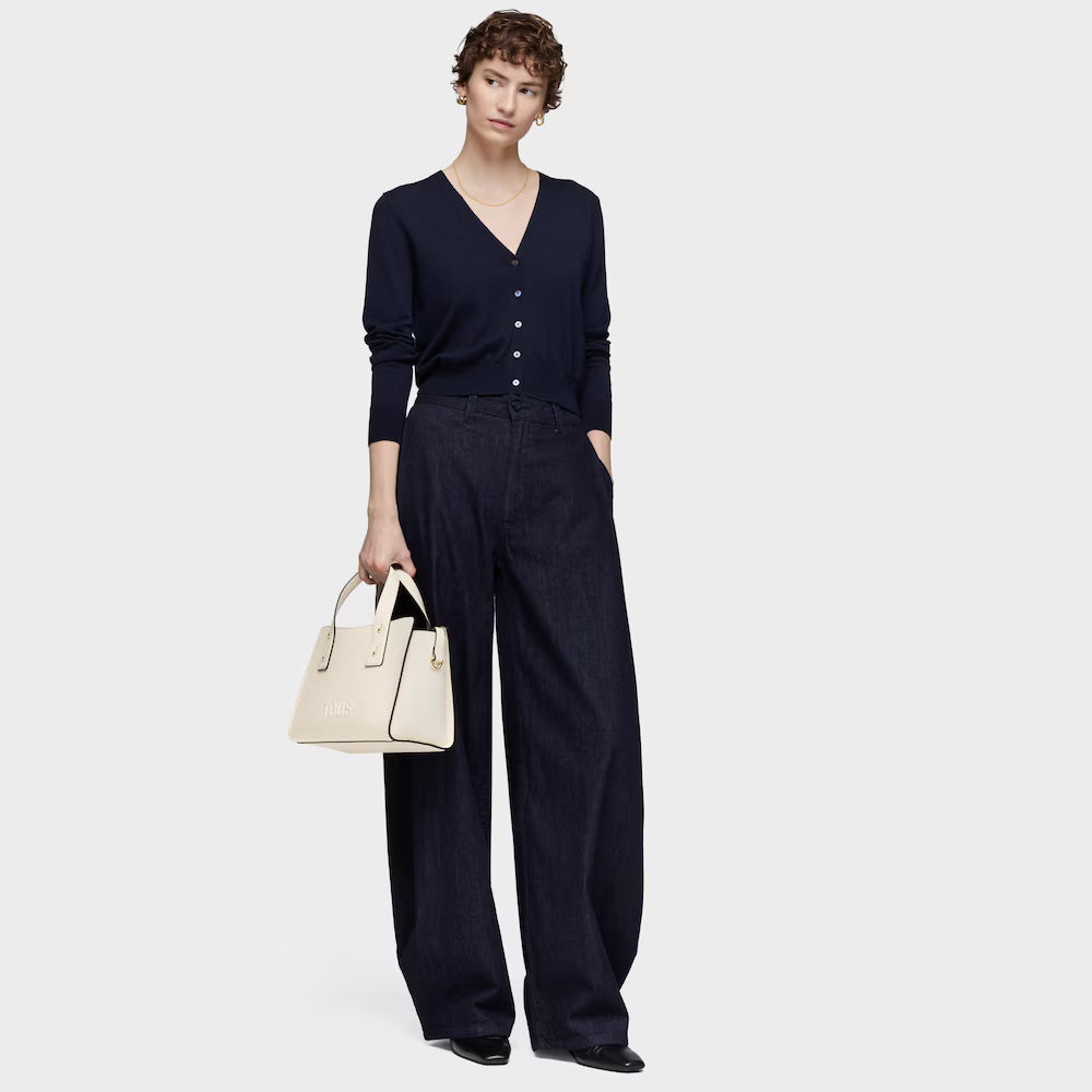 אישה לובשת סריג שחור ומכנסיים מחויטים רחבים, נושאת תיק יד אופנתי בצבע שמנת