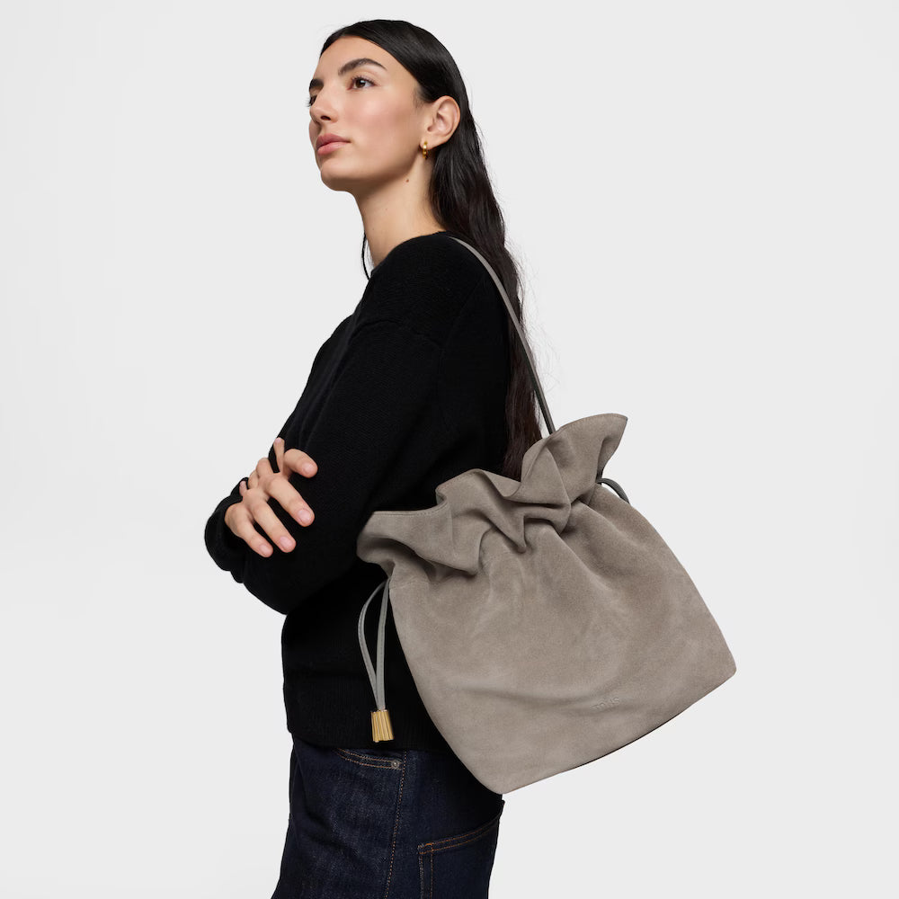 אישה עם תיק גב אופנתי מבד זמש אפור, לבושה בסוודר שחור ומכנסי ג'ינס