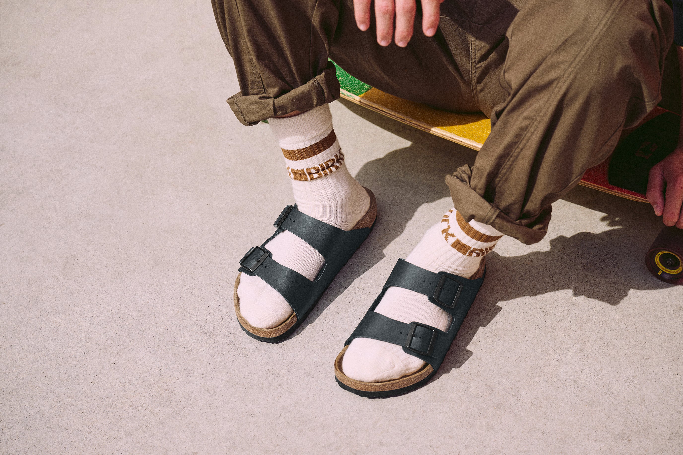 נעליים פתוחות בירקנשטוק שחורות עם גרביים לבנות, מכנסיים חאקי, ליד סקייטבורד על כביש, CHOZEN מותגים