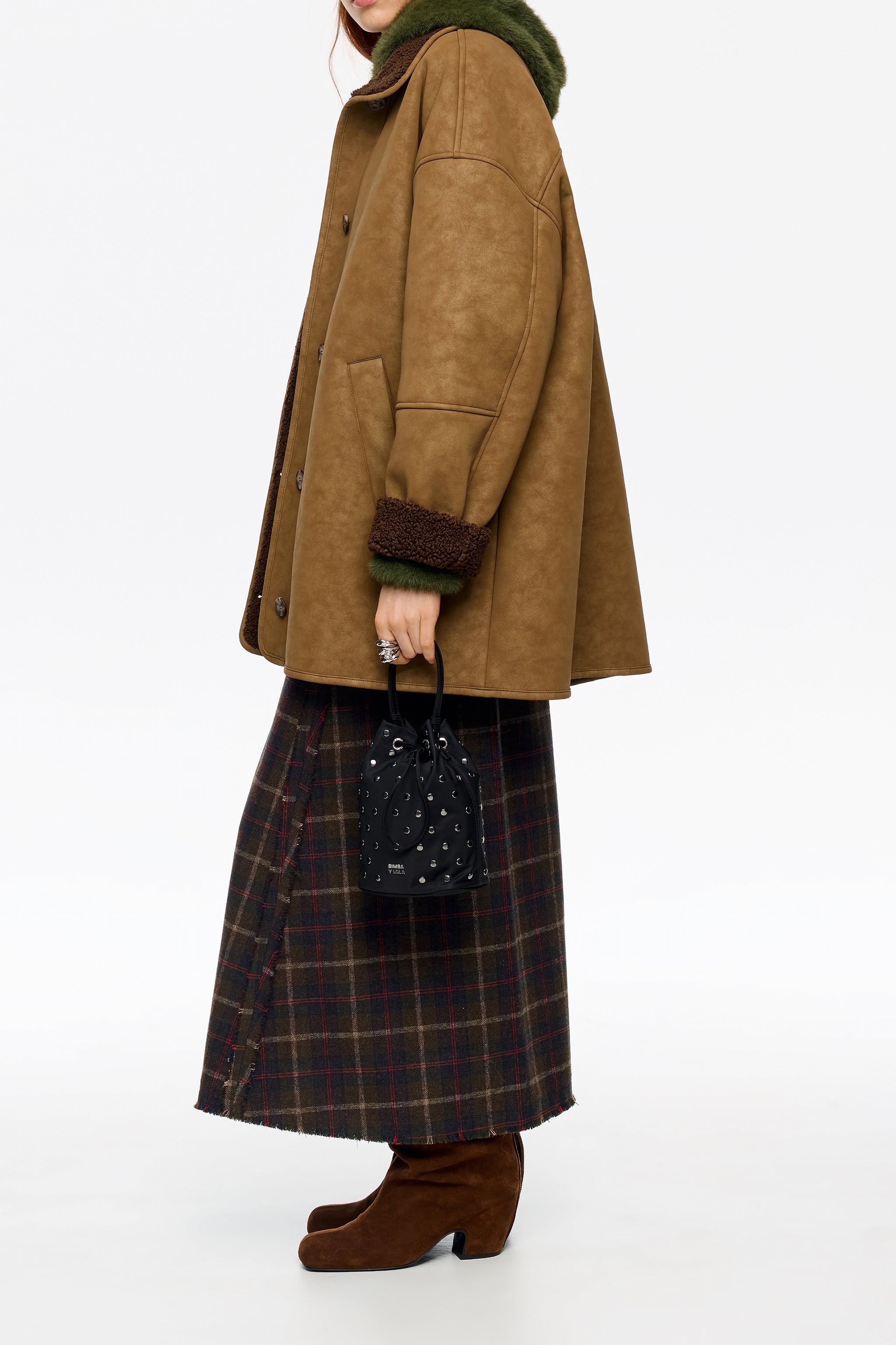 מעיל חום אופנתי עם צווארון ירוק פרוותי, חצאית משובצת, תיק שחור ונעלי זמש חומות, מבית CHOZEN