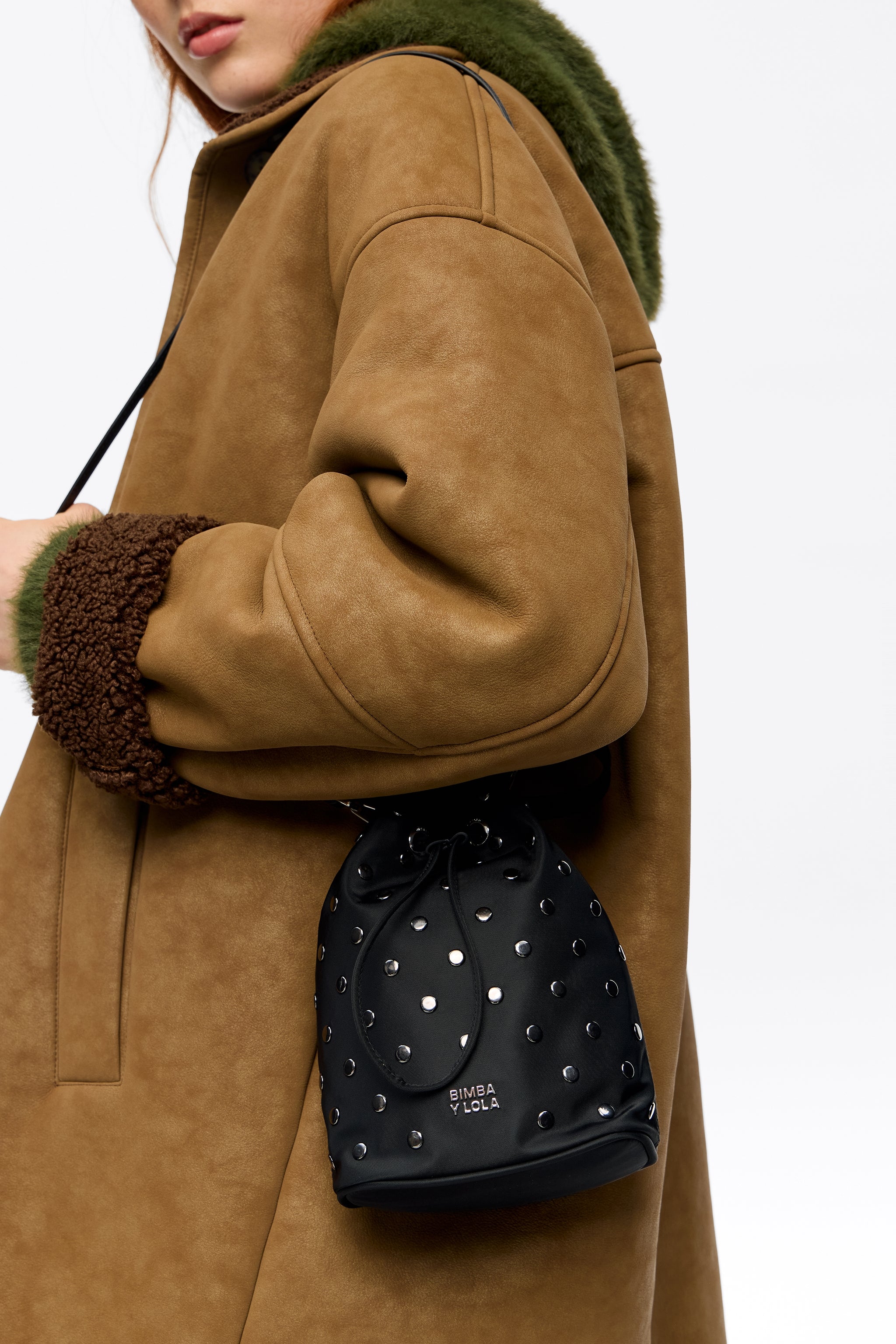 אישה במעיל חום עם פרווה ירוקה, תיק עור שחור ממותג Bimba Y Lola, אופנת חורף CHOZEN