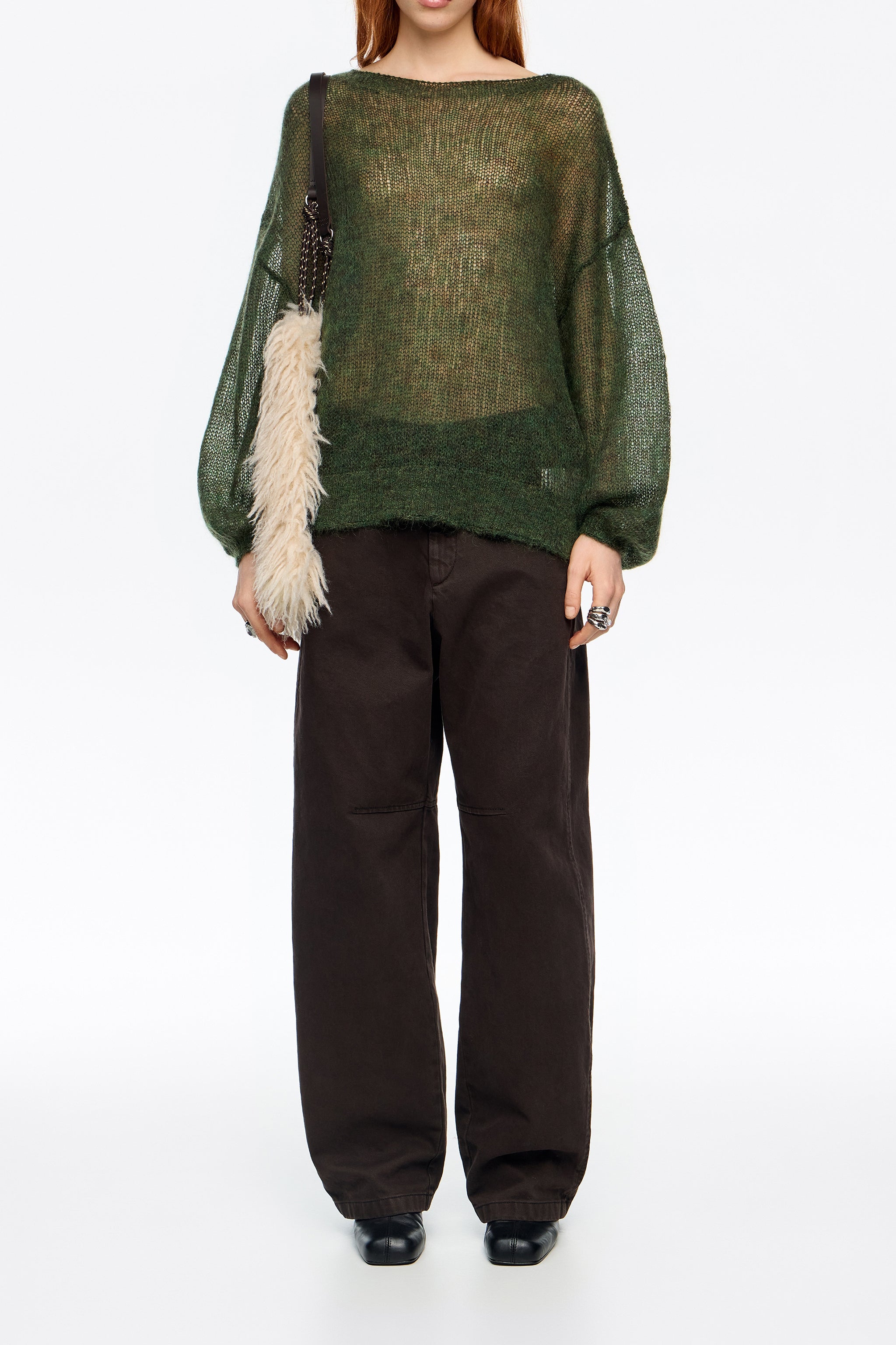 אישה עם סוודר ירוק שקוף, מכנסיים שחורים רחבים ותיק עם רצועת פרווה, אופנת CHOZEN