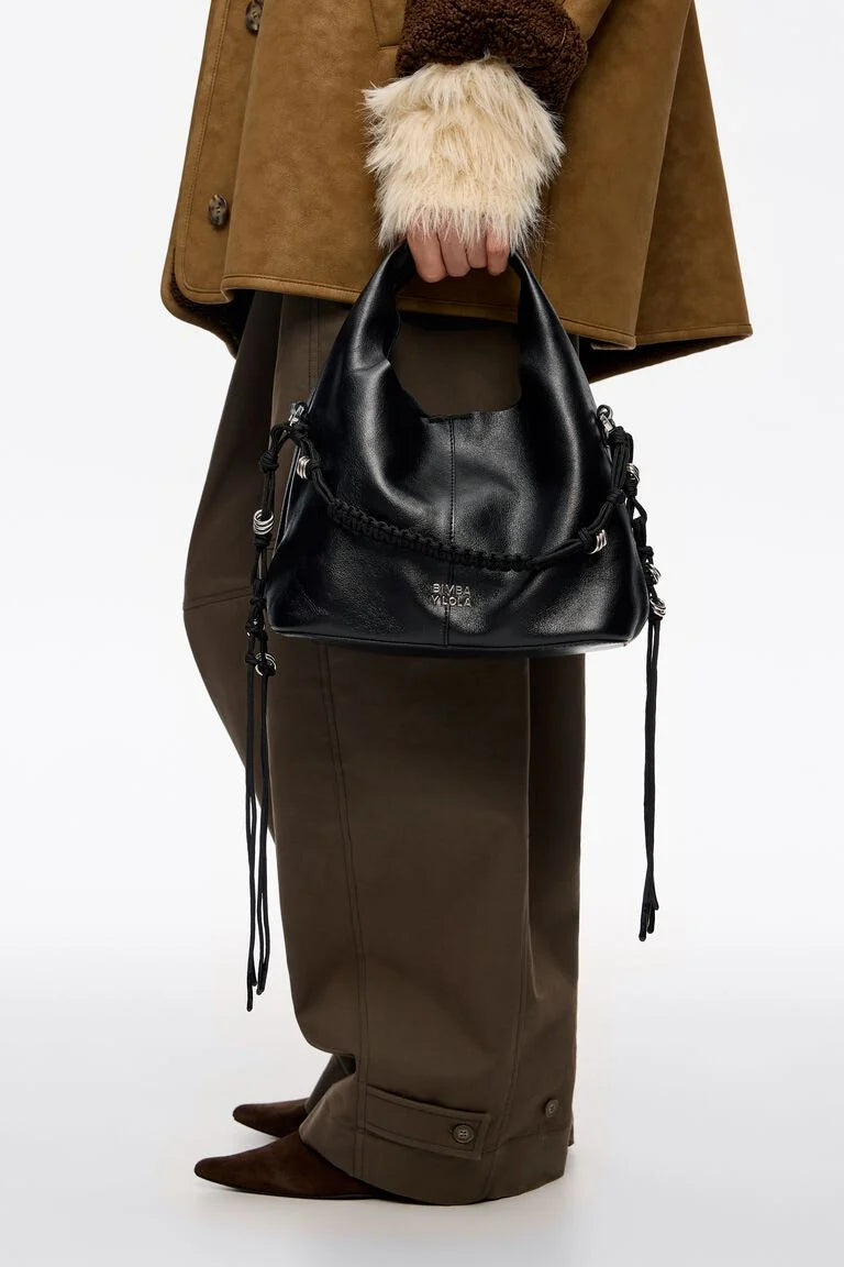 תיק עור שחור אופנתי עם שרוכים צדדיים, מוחזק ביד, לבוש חורפי בצבעי חום