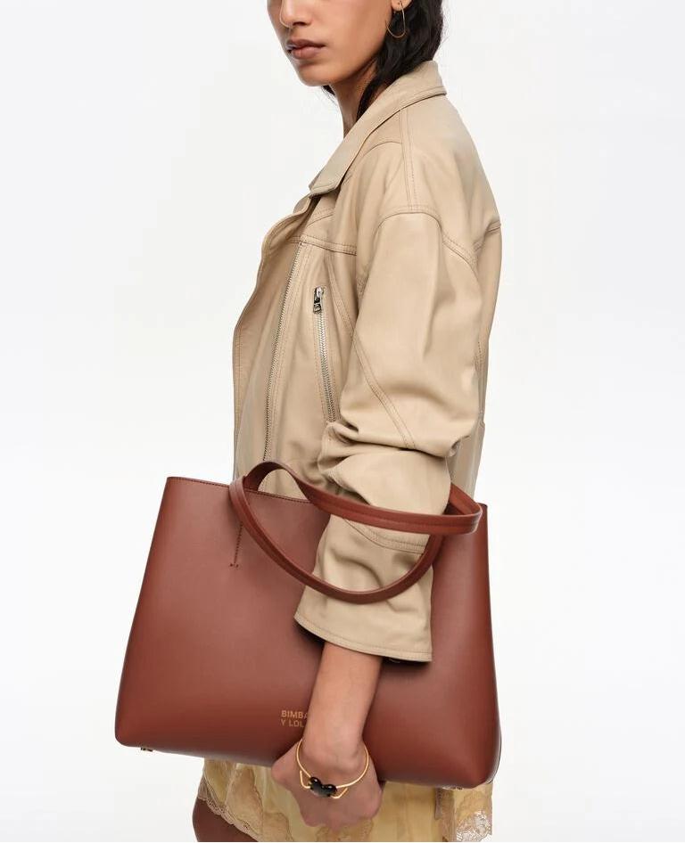 אישה עם תיק עור חום טרנדי על הכתף, לובשת ז'קט בז', צילום אופנה