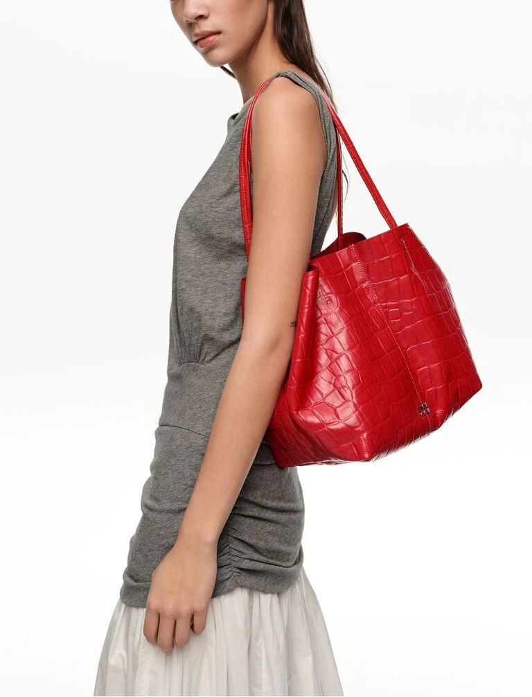 אישה לובשת שמלה אפורה נושאת תיק צד אדום דמוי עור תנין על הכתף