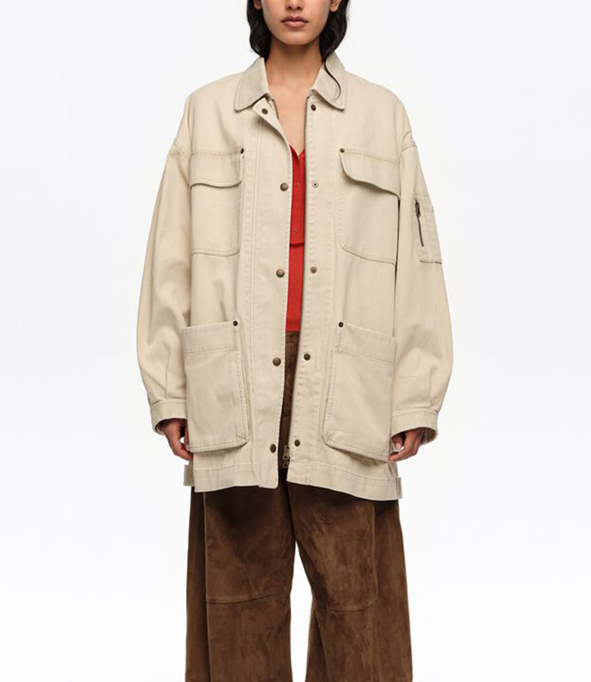 אישה לובשת מעיל בז' עם כפתורים וכיסים גדולים, חולצה אדומה ומכנסי חום רחבים