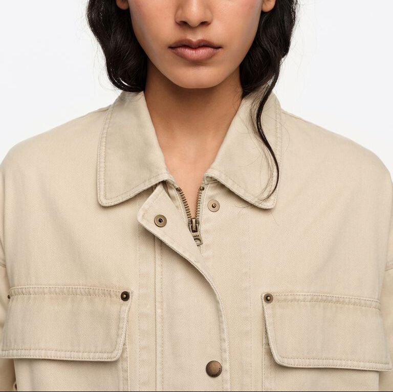 אישה לובשת ז'קט בז' עם כיסי חזית, רוכסן וכפתורים, צילום אופנה מקרוב