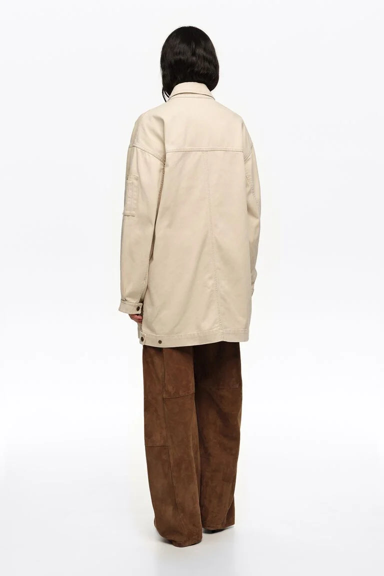 אישה לובשת מעיל בגוון שמנת ומכנסיים חומים רחבים, צילום מהגב על רקע לבן