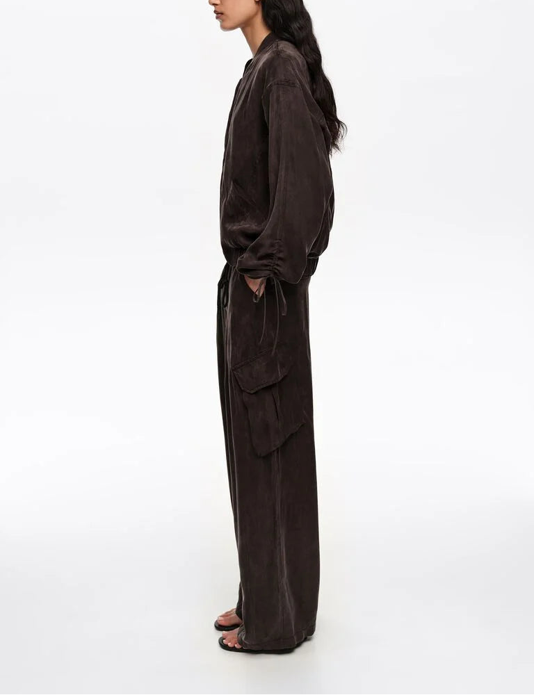 אישה לובשת חליפה רחבה בצבע חום כהה, מכנסיים עם כיסי צד, חולצה ארוכה, צילום צד